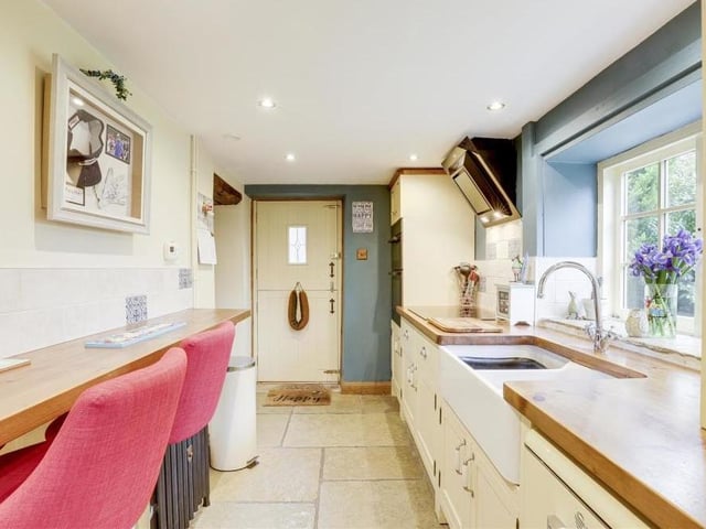 The kitchen boasts a range of fitted, shaker-style base and wall units with wooden worktops. Additional assets include flagstone flooring, recessed spotlights, a cast-iron column radiator, two wood-framed sash windows and a stable door,