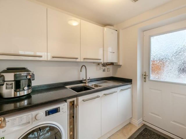 Just off the kitchen is this utility room, with space and plumbing for a washing machine. It features high-gloss wall and base units, work surfaces and an inset one-and-a-half-bowl stainless steel sink with drainer and mixer tap. The room houses a wall-mounted gas central heating boiler too.