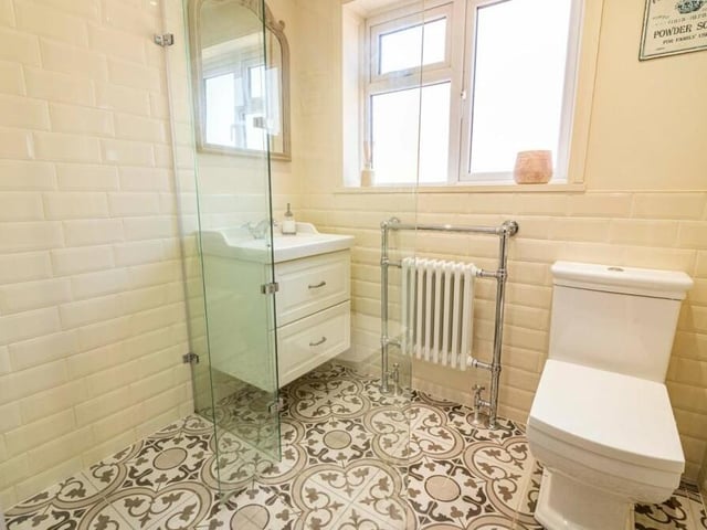 The first floor is completed by this family wet room, which is made up of a three-piece suite in white. There is a wall-mounted dual rainfall-effect shower, vanity sink unit, WC, heated towel-rail, ceiling spotlights and tiled flooring.