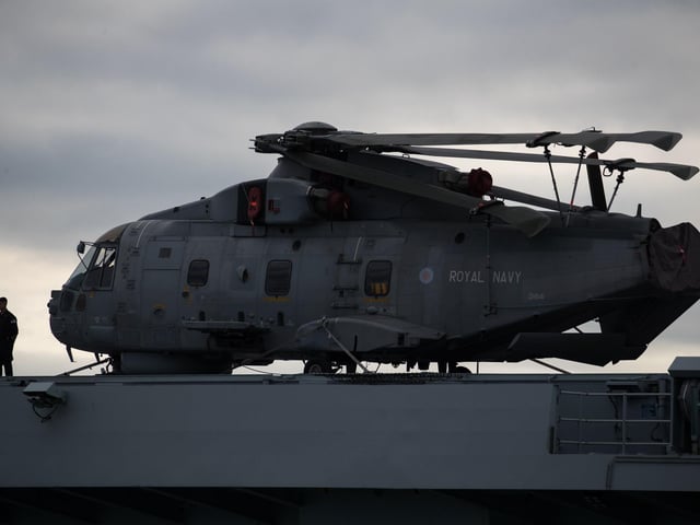 A crew member stands next to a Merlin helicopter on the flight deck of HMS Queen Elizabeth as she leaves Portsmouth on September 9. Picture: Andrew Matthews/PA Wire