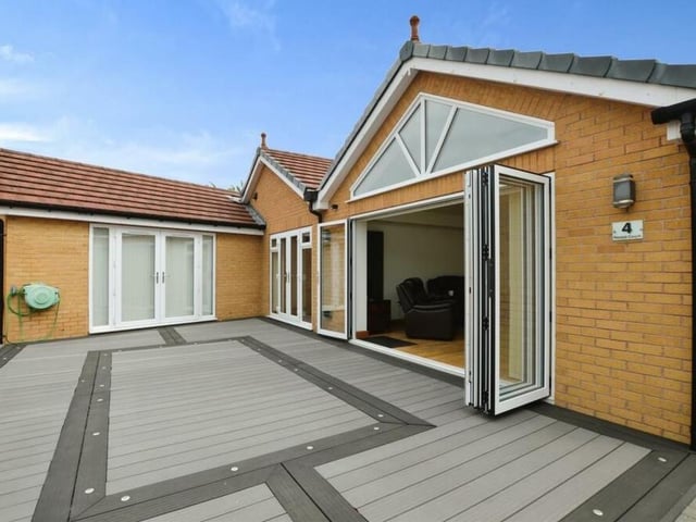 Let's step outside now, starting with this patio seating area at the front of the property. You can see how the large doors from the living room open on to it.