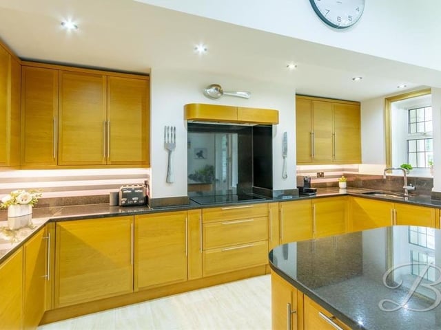 The contemporary kitchen from a different angle. A range of integrated appliances include three ovens and a warming drawer, fridge freezer and dishwasher. There is also a ceramic hob, extractor fan and inset sink with chrome mixer tap above.