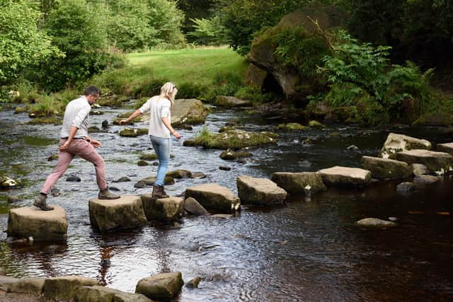Visitors crossing stepping stones at Hardcastle Crags, West Yorkshire. Hardcastle Crags is a beautiful wooded valley with deep ravines, tumbling streams and glorious waterfalls.