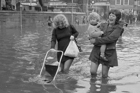 Managing to make light of the knee-deep water that has flooded Bridge Street back in 1976.