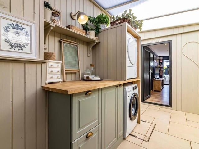 A door from the dining kitchen leads to this cute utility room, where there is space and plumbing for a washing machine. It has a polycarbonate roof, tiled floor, stainless steel sink and fitted cupboards, while French doors lead to the garden and doors lead to the car port and garden room.