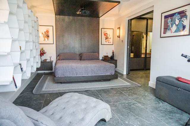 The main bedroom has sliding black glass privacy doors with a built-in wooden bed. A balcony overlooks the garden. The bedroom is linked to a dressing area with floor to ceiling mirrored wardrobes and an illuminated mirrored dressing table, and an en-suite bathroom.