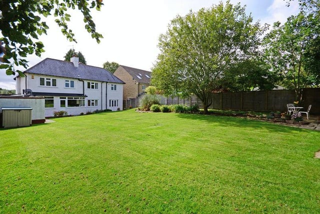 The back garden contains shrubs, bushes, trees and a large lawn enclosed by fencing and hedging.