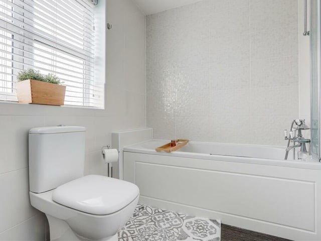 Completing our inspection of the first floor is this family bathroom. A three-piece suite includes a low-level, dual-flush WC and a panelled bath with wall-mounted shower fixture and bi-folding shower screen.
