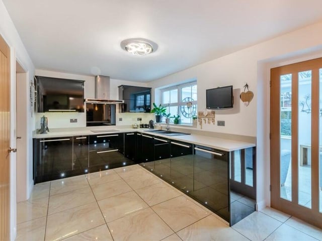 The kitchen cabinets comprise wall cupboards with under lighting, and base units with kickboard lighting and drawers. Quartz-effect work surfaces feature a contoured, integrated sink with a mixer tap and drainer to one side.