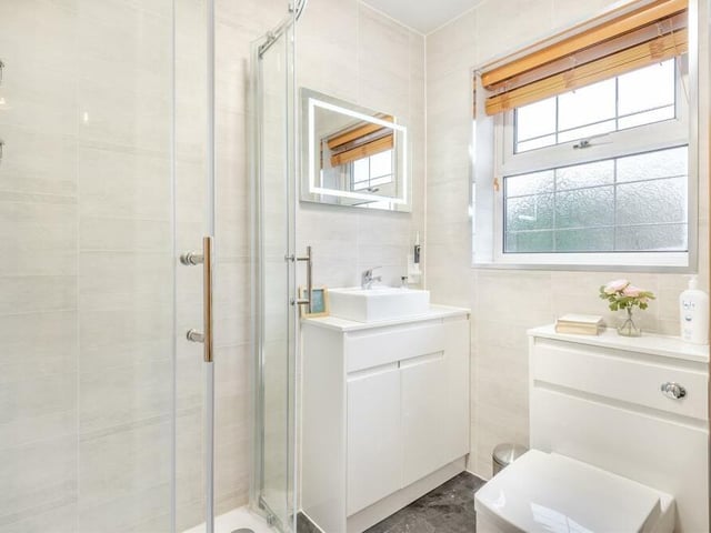 This is the en suite shower room to the master bedroom. A modern white suite comprises a shower enclosure with rainfall shower and an additional handset, vanity unit with inset wash hand basin with mixer tap and storage cupboard beneath, and a low-flush WC. There is also a fitted, heated mirror above the sink with touch-screen lighting, and a heated towel-rail.