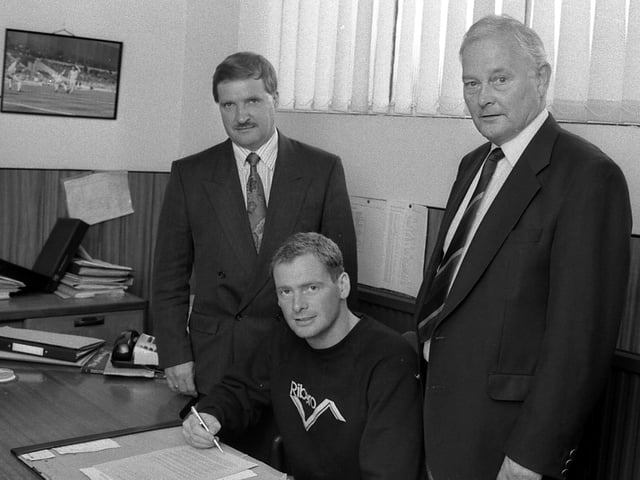Phil Stant signs with managing director Geoff Hall and secretary Joe Eaton looking on.