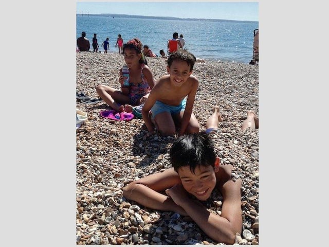 Joshua Johnson, 10, wears a smile as he's buried in the stones by his pal, Alberto, who is also 10. Joshua's sister Alexandra, eight, is also pictured. Picture: Layla Johnson