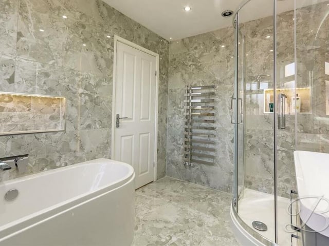The family bathroom is a sparkling four-piece designer suite, featuring a fitted bath with waterfall tap and built-in TV, walk-in corner shower unit and chrome, heated towel-rail.