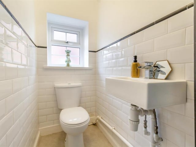 Next to the shower room is this additional toilet, including a wash hand basin with chrome 'waterfall' mixer tap and low-flush WC. Contemporary tiles adorn the walls.