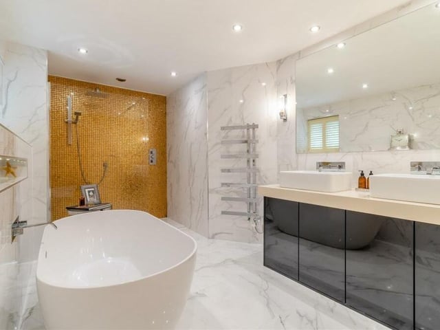 Completing our look at the first floor is this fabulous family bathroom, complete with chrome fittings. It consists of a bath tub, separate walk-in shower area with rainfall shower, feature gold tiling and recess area with inset lighting, large vanity unit with his and hers sinks and storage beneath, and a wall-hung, low-flush WC. A marble-style tiled floor and walls, underfloor heating, a heated towel-rail and ceiling spotlights add to its appeal.
