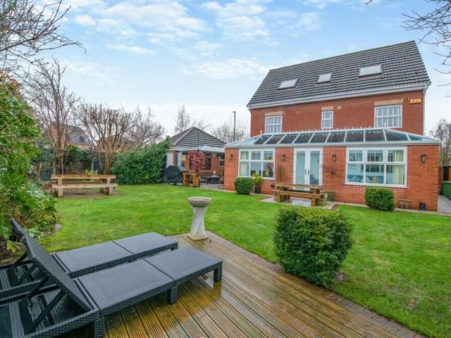 As we step outside, let's take in a view of the rear of the house from its glorious garden. You can see how the conservatory runs the length of the building and how a central lawn features a decked patio.