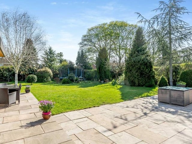 Another shot of the patio and lawn, which are surrounded by well-stocked borders with mature shrubs and trees.