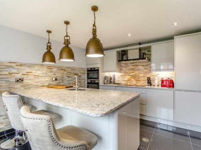 Next stop on our tour is the beautifully appointed, modern fitted kitchen. High-gloss, light grey cabinets comprise wall cupboards, base units and drawers, complemented by quartz worktops. There is a large island/breakfast bar and inset one-and-a-half-bowl stainless steel sink with filtered water tap.
