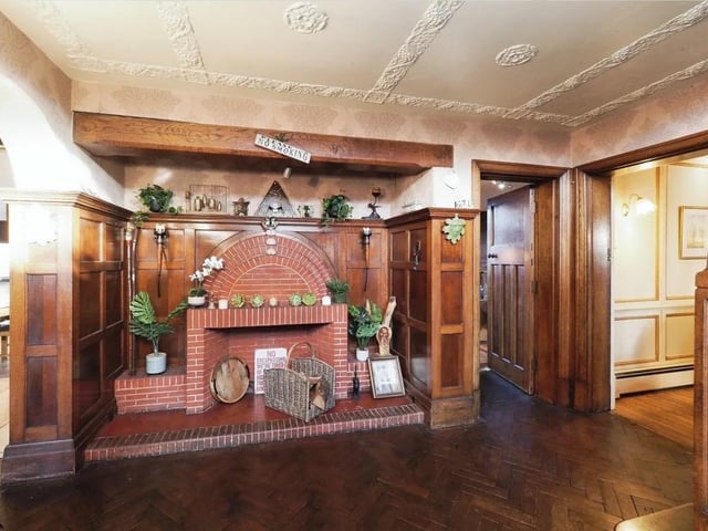 The grand reception hall features parquet tiled flooring, a feature brick fireplace with built-in cupboards, and stairs to the first-floor galleried landing.