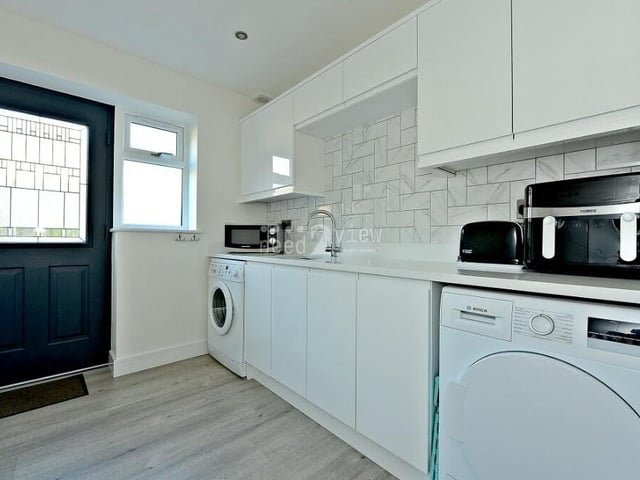 By the kitchen diner, you will find this handy utility room. It features a wash basin, space for both a washing machine and a tumble dryer, additional pantry space, a grey laminate floor and ceiling spotlights.