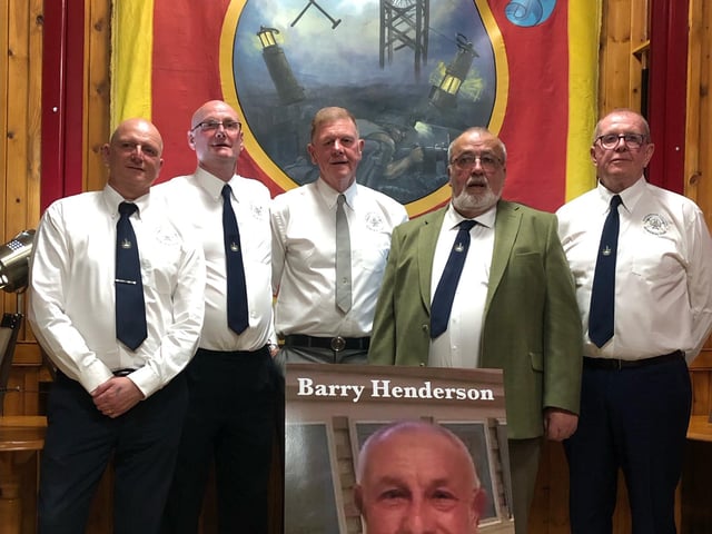 A committee of ex-miners formed for the planning of the statue. Here members pose for a photo with the restored Derbyshire Area NUM banner, alongside a photo of the late Barry Henderson, who brought forth the idea of a commemorative statue to honour the area's fallen miners.