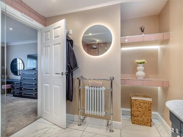 Featuring a contemporary three piece white suite comprising a walk-in shower with large rainfall ceiling mounted shower. Vanity unit with inset wash hand basin with mixer tap, quartz marble style work surfaces and storage cupboard beneath. Low flush WC. Marble style tiled floor, electric underfloor heating, six ceiling spotlights, alcove area with tiled shelving, radiator, heated mirror with inset LED lighting and obscure double glazed window to the rear elevation.