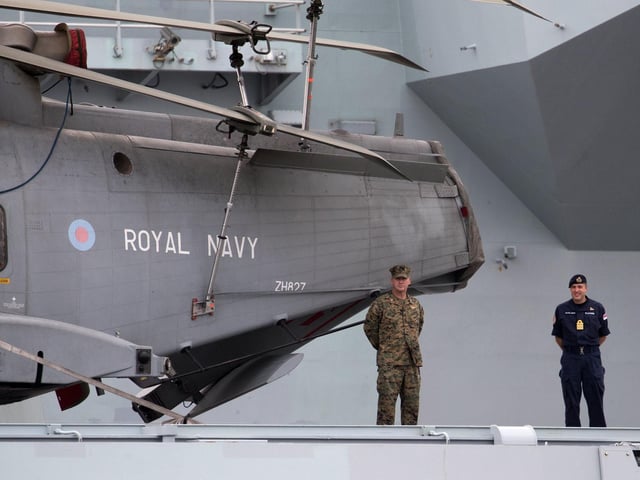 A Royal Navy officer and a member of the US Marines stand next to a Merlin helicopter on the flight deck of HMS Queen Elizabeth. Picture: Andrew Matthews/PA Wire