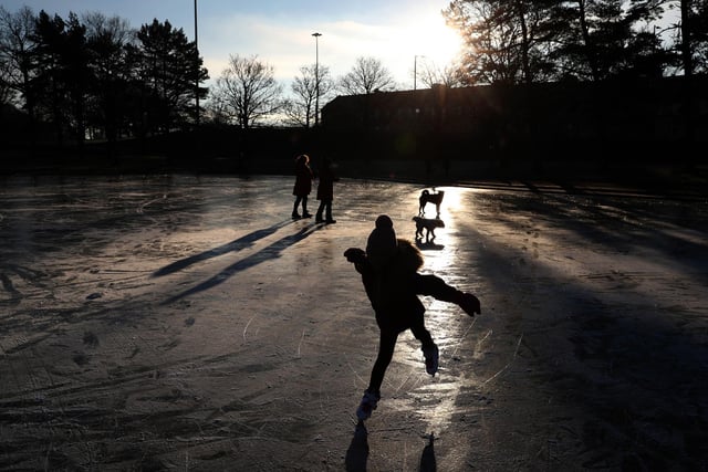 People skate and walk their dogs on a frozen pond at Victoria Park in Glasgow.