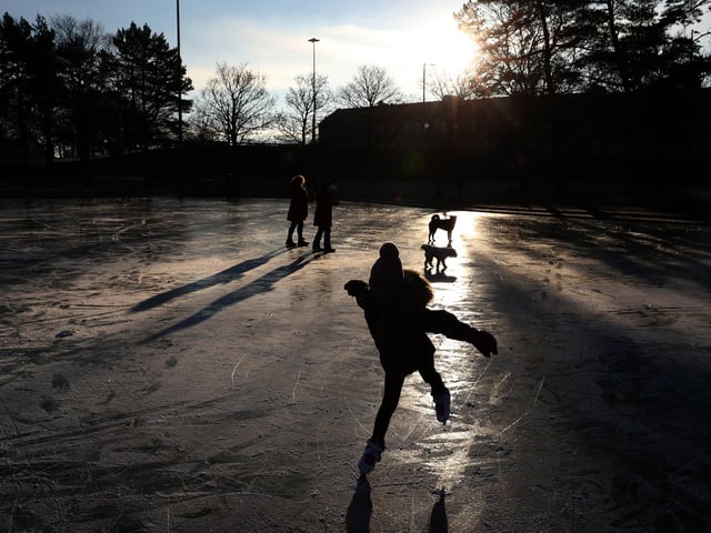 People skate and walk their dogs on a frozen pond at Victoria Park in Glasgow.