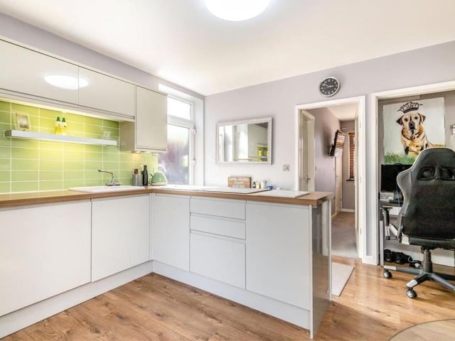 A second view of the kitchen/diner in the annexe. There is a range of modern, high-gloss cabinets and an inset one-and-half-bowl ceramic sink with mixer tap, while a recess storage cupboard to the right is currently being utilised as a study area.