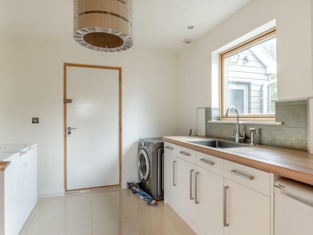Just off the kitchen is this handy utility room, which has space for a freezer and plumbing for a washing machine. Modern, high-gloss white cabinets comprise base units and drawers with a cocobolo worktop above, incorporating a stainless steel sink. This room also houses the property's gas boiler.