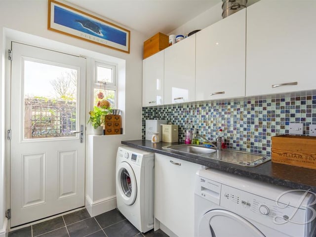 Complete with a range of modern gloss units and cabinets with inset sink and drainer. With space and plumbing for a washing machine and tumble dryer and there is a door leading outside.
