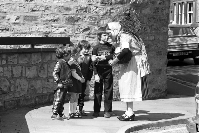 With her basket on her back, traditionally-dressed fishwife Nan Oliver takes her seafood and shellfish round the Trinity area of Edinburgh in May 1982. These children seem unsure of the cockles she offers them.