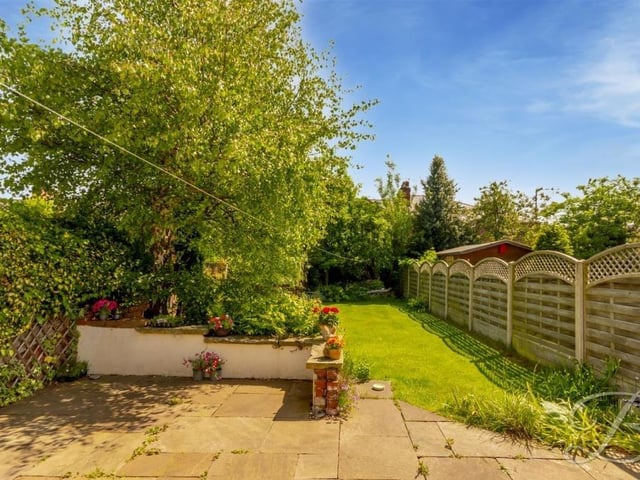 A south-facing garden at the back of the Mansfield house that mixes a tiled patio space with a well-maintained lawn and decorative shrubbery.