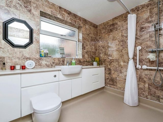 Before we take a look at the third bedroom, here is the large and striking wet room. It features a mains-fed shower, low-level WC, pedestal wash hand basin built into a vanity unit with storage, fully-tiled walls and a vinyl floor.