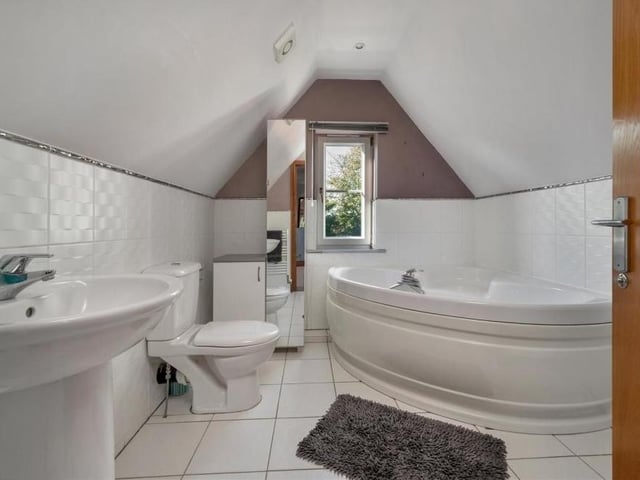 The en suite bathroom to the second-floor bedroom features a large corner bathtub with mixer tap and shower handset, plus a pedestal wash hand basin, low-flush WC, heated towel-rail and fitted base unit with worktop above.
