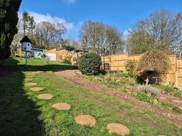 To the rear is a private garden with various paved patio seating areas, a lawn, mature shrubs and trees, a variety of plants, a wildflower meadow, a mini orchard and a shed.