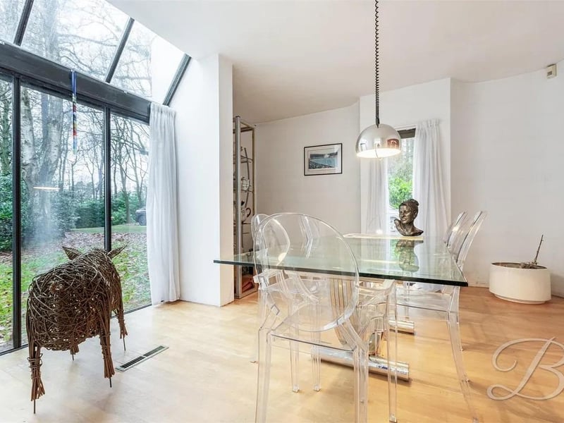 The dining room features dual-aspect floor-length windows flooding the space with natural light while framing stunning views of the surrounding plot, creating a seamless connection to the outdoors.