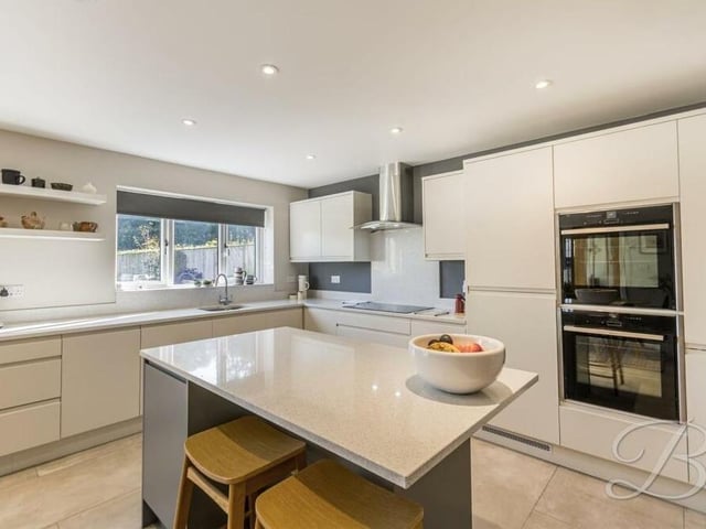 Surrounding an island, which has extra storage and worktop space, is a range of integrated appliances. These include a double electric oven, a fridge freezer and a dishwasher.