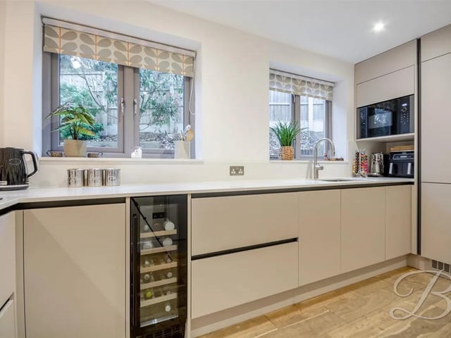 The kitchen features quality solid wood flooring, matching sleek cabinets and ample worktop space, featuring integrated appliances including oven, microwave, wine cooler, and fridge/freezer.