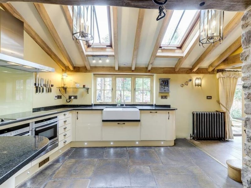 The kitchen features a modern range of fitted base units with worktops, and a double Belfast sink with a swan-neck mixer tap. Note how the Velux windows flood natural light into the space.