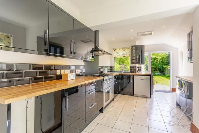 The kitchen features a built-in oven with hob and extractor fan above, plus an inset sink and drainer with mixer tap and splash tiling. A tiled floor, downlighting and matching gloss wall and base cabinets add to its smart appearance.