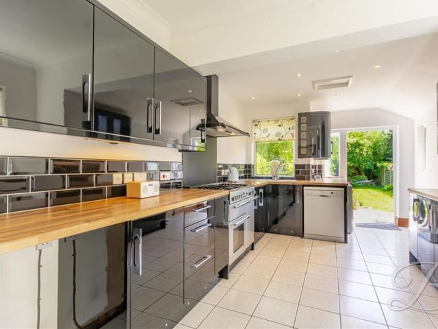 The kitchen features a built-in oven with hob and extractor fan above, plus an inset sink and drainer with mixer tap and splash tiling. A tiled floor, downlighting and matching gloss wall and base cabinets add to its smart appearance.