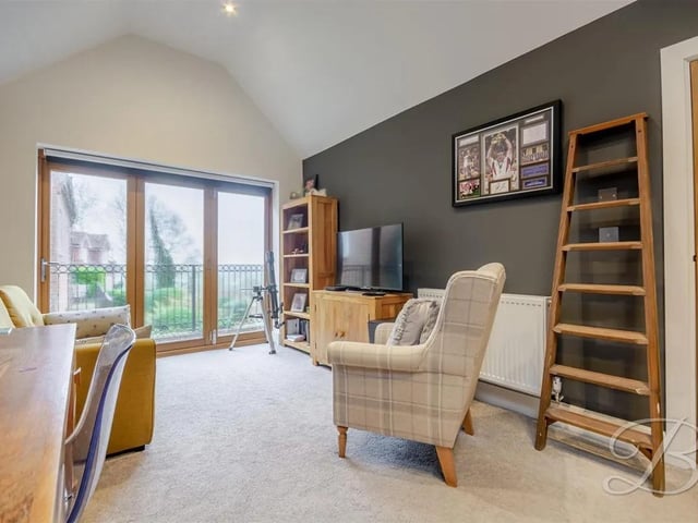 The spacious carpeted living room features a built-in wardrobe, offering practical storage and bifold doors to the front opening onto a balcony, providing plenty of natural light and a pleasant outdoor space to enjoy the view. The room is bright, airy, and versatile, ideal for relaxation or entertaining.