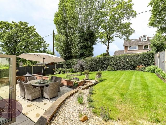 The rear garden is enclosed and enchanting in equal measure. Bordered by hedges and timber fences, it features a turfed lawn, and a range of trees, plants, shrubs and flowerbeds.
