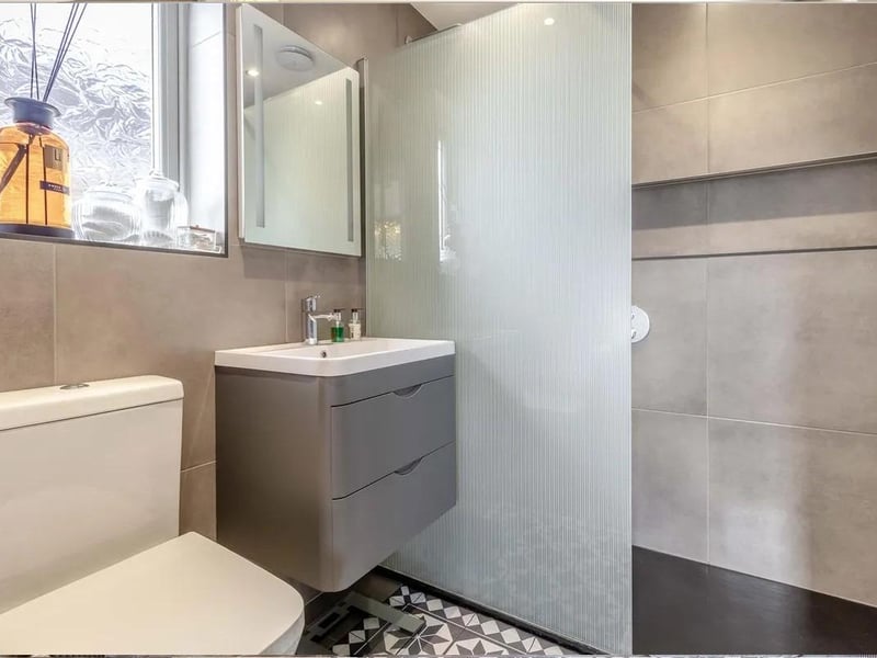 Having a modern three piece white suite comprising a walk-in tiled shower with wall mounted rainfall shower plus additional shower attachment. Vanity unit with inset wash hand basin with mixer tap and two storage drawers beneath. Low flush WC. Tiled walls, contemporary towel rail, four ceiling spotlights, extractor fan obscure double glazed window to the side elevation.