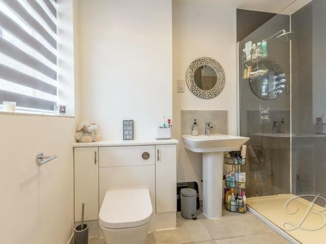 Here is the contemporary en suite shower room to bedroom two. It comprises an enclosed shower, pedestal sink, low-flush WC, tiled floor and an opaque window.