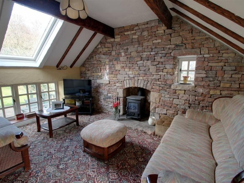 Next stop on our tour is the property's annexe/cottage, at the heart of which is this unique sitting room. It displays period features, including exposed stonework and beams to the ceiling, while windows to three aspects provide natural light and a gas stove adds extra character.
