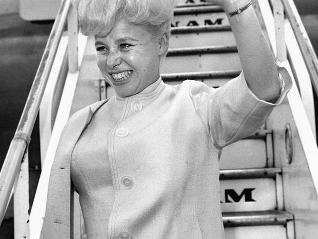 Barbara Windsor, waving farewell before leaving London Airport for her first ever visit to the United States in 1963.