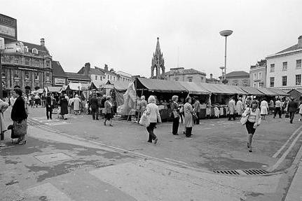 A busy market place full of stalls and shoppers.